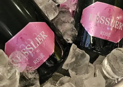 Zwei Flaschen Kessler Rosé Sekt mit pinken Etiketten in einem Eiseimer, umgeben von Eiswürfeln.