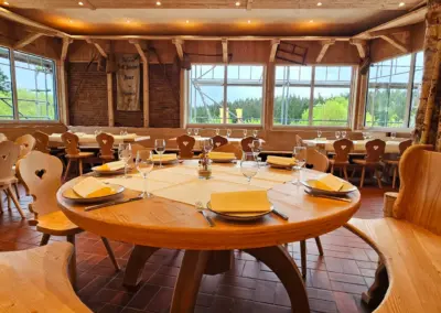 Rundes Holztisch-Set mit eingedeckten Plätzen in einem Restaurant mit großen Fenstern und Holzwänden.