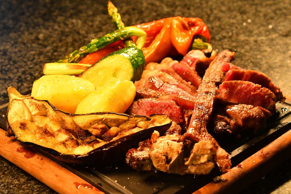Holztisch mit vier gelb gefalteten Servietten und weißen Tischsets in einem Restaurant mit großen Fenstern und Pflanzen auf der Fensterbank.